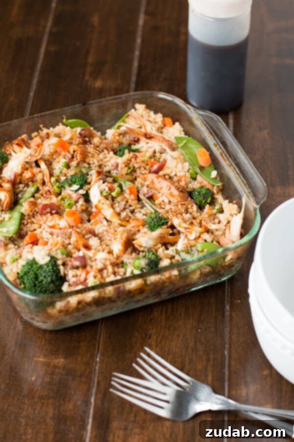 The Best Teriyaki Chicken Casserole 3 A square glass casserole dish filled to the brim with Teriyaki Chicken Casserole, showcasing golden fried rice, succulent pieces of teriyaki chicken, and an assortment of colorful, crisp-tender vegetables.