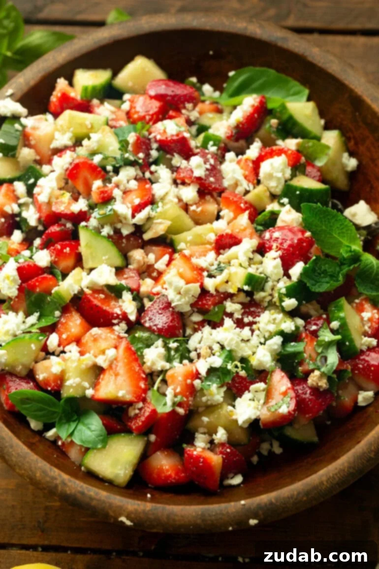 Refreshing Strawberry Feta Salad with Lemon, Cucumber, Basil and Mint 2 A large wooden bowl brimming with vibrant strawberry cucumber salad, adorned with crumbled feta and fresh basil and mint leaves.