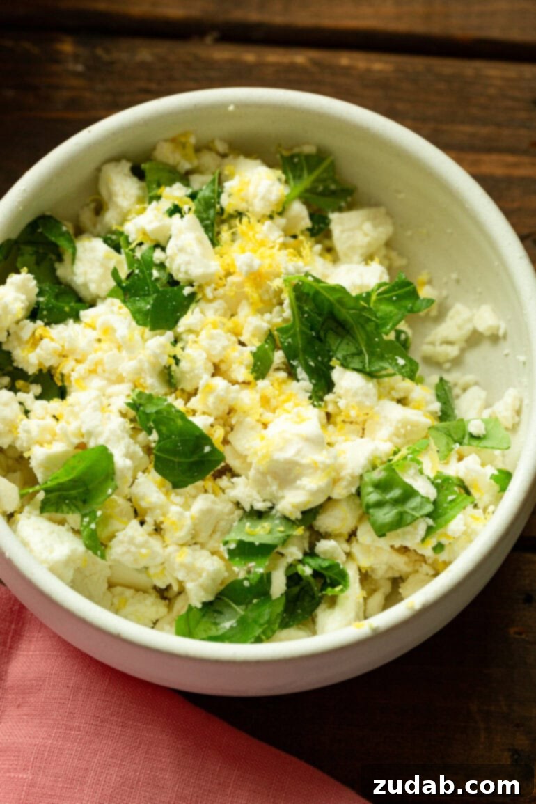 Refreshing Strawberry Feta Salad with Lemon, Cucumber, Basil and Mint 4 Close-up shot of crumbled feta cheese being tossed with fresh lemon zest, chopped basil, and mint, preparing the flavorful base for the salad.