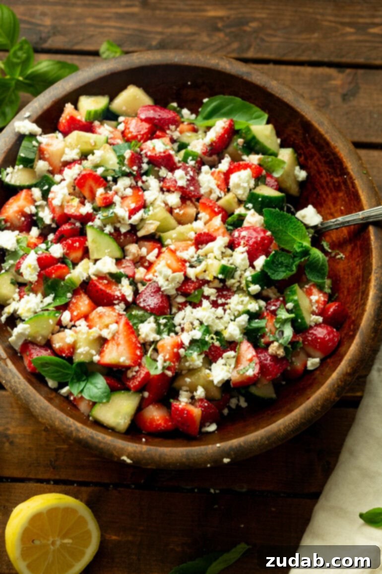 Refreshing Strawberry Feta Salad with Lemon, Cucumber, Basil and Mint 6 A close-up view of the prepared cucumber and strawberry salad, garnished with crumbled feta, fresh basil, and mint, glistening with honey balsamic dressing.