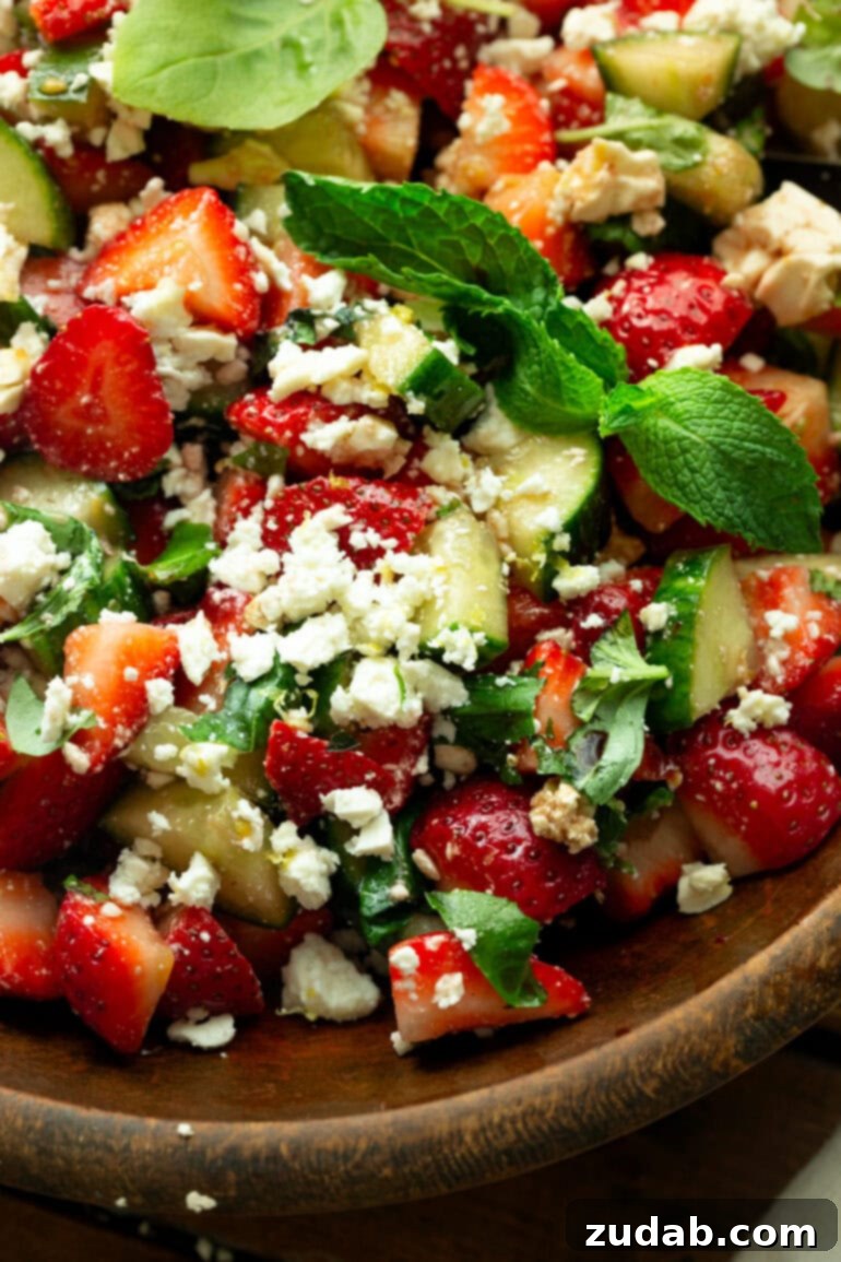 Refreshing Strawberry Feta Salad with Lemon, Cucumber, Basil and Mint 7 An overhead shot of a delightful strawberry cucumber salad, mixed with crumbled feta and fresh herbs, presented beautifully in a large wooden bowl.