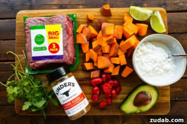 A top-down view of all fresh ingredients laid out for a high-protein cottage cheese beef and sweet potato bowl, including cubed sweet potatoes, avocado, cottage cheese, cooked ground beef, cilantro, cherry tomatoes, and various seasonings.