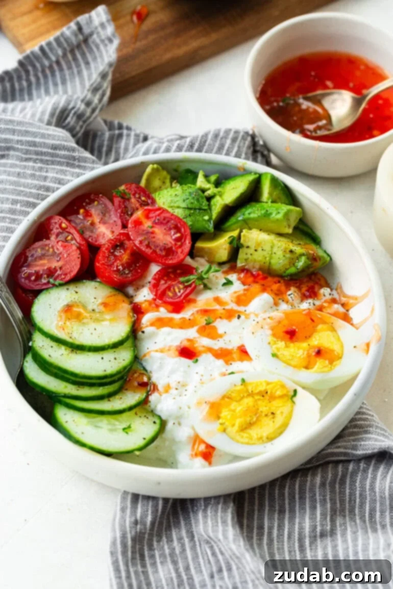 The Ultimate Protein Power Bowl 2 A large bowl filled with creamy cottage cheese, perfectly sliced hard-boiled eggs, crisp cucumber, vibrant cherry tomatoes, and creamy avocado, finished with a drizzle of sweet chili sauce.
