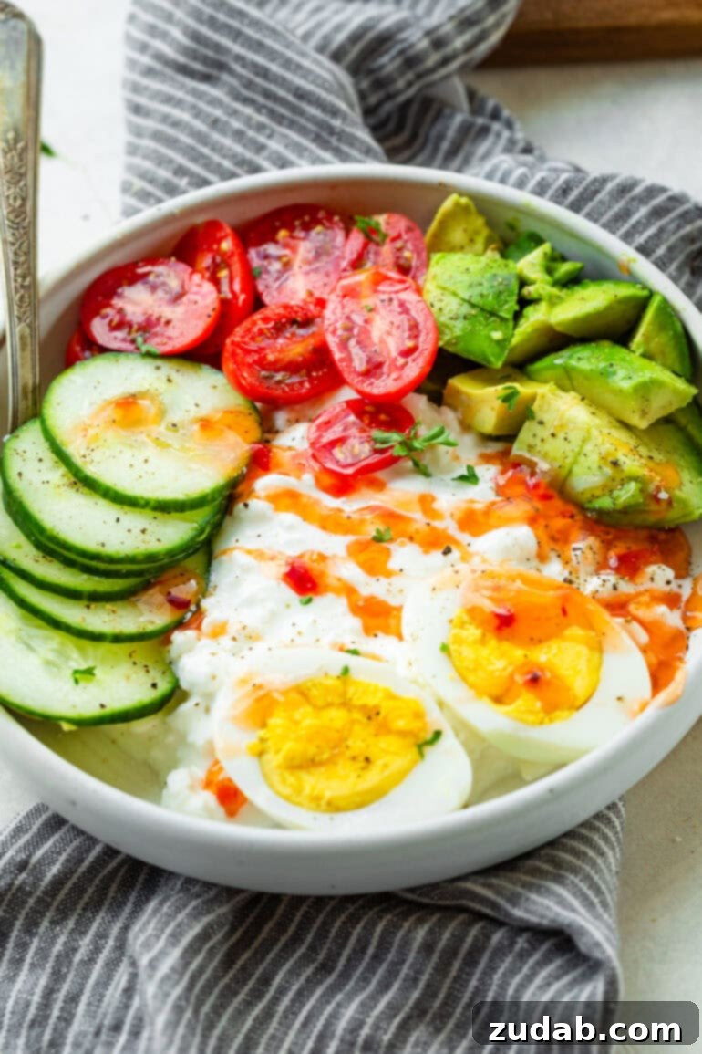 The Ultimate Protein Power Bowl 5 A beautifully composed high-protein breakfast bowl featuring creamy cottage cheese topped with sliced hard-boiled eggs, fresh avocado, crisp cucumber, and bright cherry tomatoes, all drizzled with sweet chili sauce.