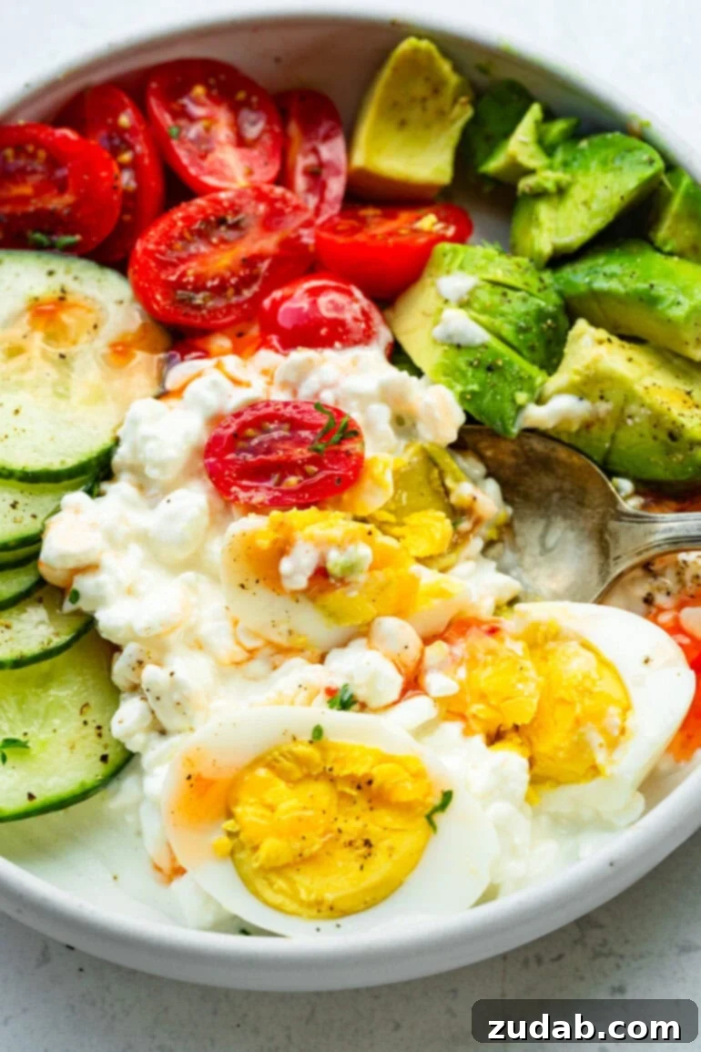 The Ultimate Protein Power Bowl 6 A delicious savory cottage cheese breakfast bowl topped with halved hard-boiled eggs, creamy avocado, vibrant grape tomatoes, and crisp cucumber slices, ready to enjoy.