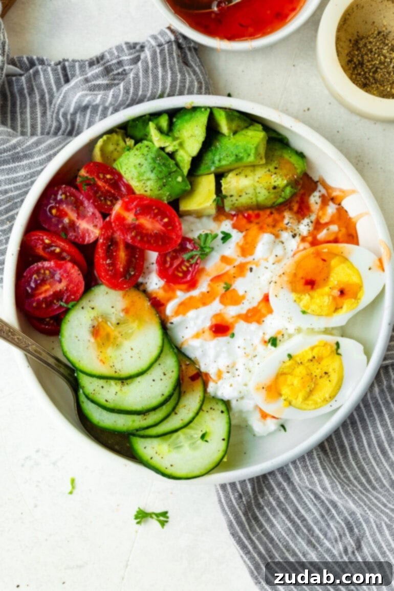 The Ultimate Protein Power Bowl 7 An inviting overhead shot of a high-protein cottage cheese and egg bowl, generously topped with slices of avocado, vibrant grape tomatoes, crisp cucumber, and a final flourish of sweet chili sauce.