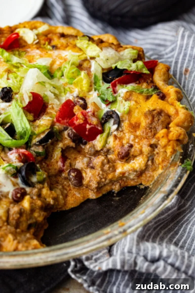 No-Fuss Weeknight Taco Pie 2 A delicious taco pie, freshly baked, topped with shredded lettuce, diced tomatoes, sour cream, and black olives, ready to be served from a pie tin.
