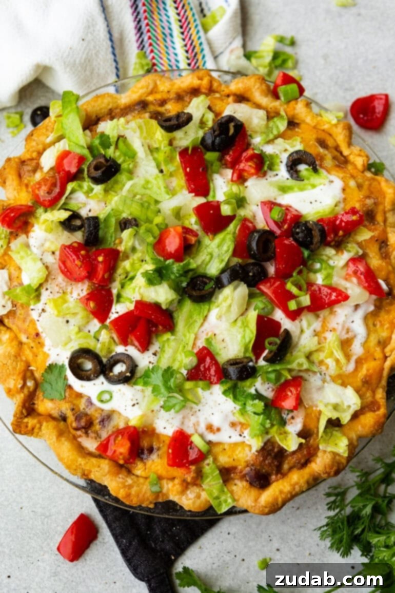 No-Fuss Weeknight Taco Pie 3 A whole, beautifully golden-crusted taco pie, generously topped with melted cheese, a dollop of sour cream, crisp shredded lettuce, fresh diced tomatoes, and sliced black olives, presented in a glass pie plate.