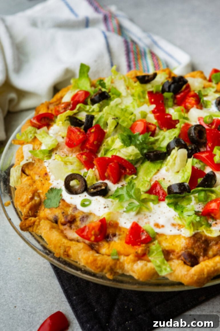 No-Fuss Weeknight Taco Pie 5 A freshly baked whole taco pie resting in a clear glass pie plate, generously topped with cool sour cream, crisp shredded lettuce, bright diced tomatoes, and savory sliced black olives.