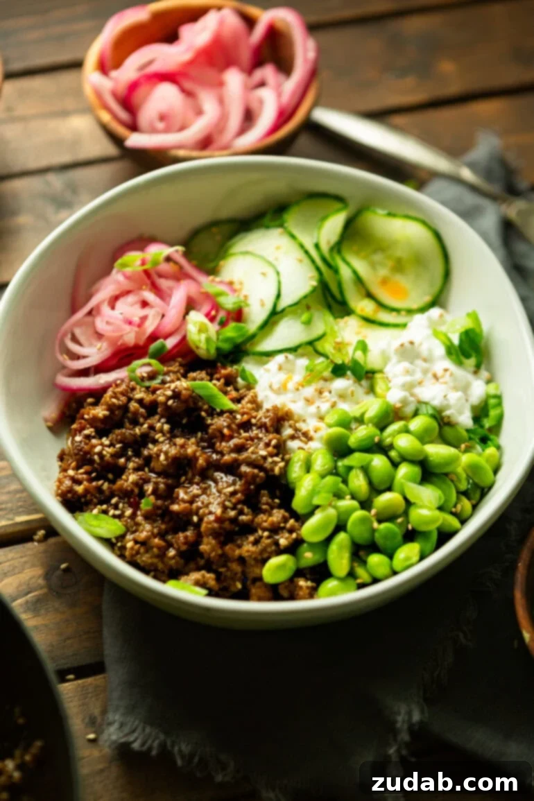Easy High Protein Korean Beef Bowl with Cottage Cheese 2 a photo of a bowl full of saucy korean ground beef with cottage cheese, edamame, pickled onions and thin slices of cucumbers