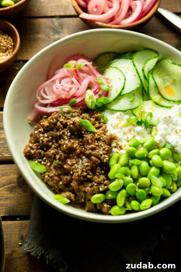 Easy High Protein Korean Beef Bowl with Cottage Cheese 5 a photo of a large white bowl full of saucy ground beef, edamame beans, cottage cheese, pickled red onions and cucumber slices