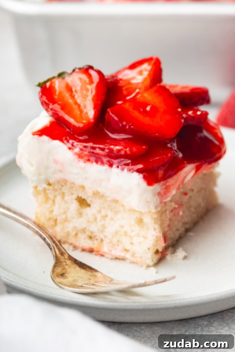Simple Strawberry Shortcake 2 A photo of a single piece of moist white cake on a small dessert plate, generously topped with creamy whipped cream cheese frosting and vibrant, juicy red strawberries. This dessert is perfect for any summer gathering.