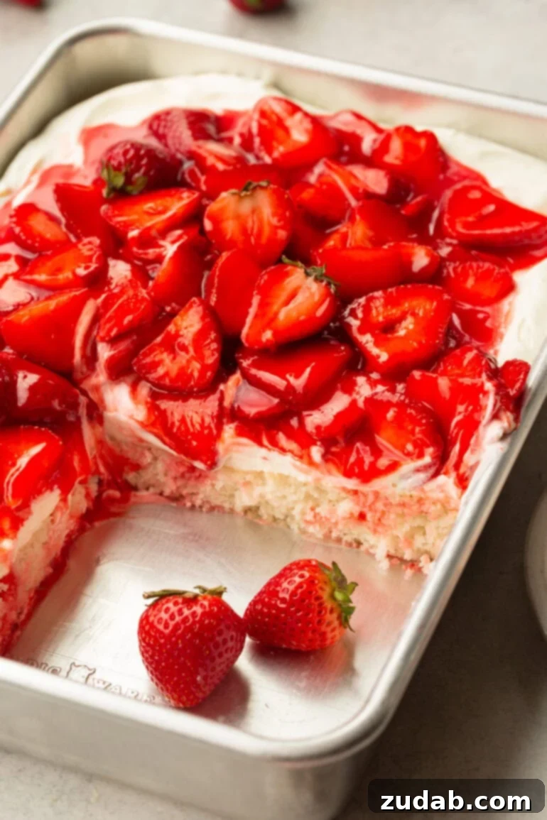 Simple Strawberry Shortcake 3 A photo of a whole strawberry shortcake cake nestled in a 9x13 inch pan, with a corner slice elegantly removed to showcase its exquisite cross-section. The cake is richly topped with juicy strawberries and a luxurious creamy frosting, inviting indulgence.