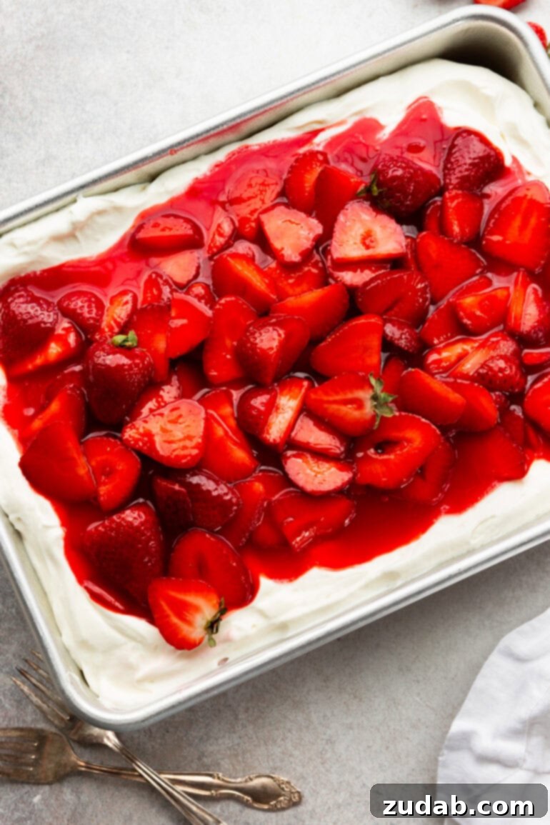 Simple Strawberry Shortcake 4 A photo of a glorious whole 9x13 inch strawberry shortcake cake, lavishly topped with creamy, cloud-like frosting and an abundance of glossy, juicy saucy strawberries. It’s a vision of summertime perfection, ready to be sliced and served.