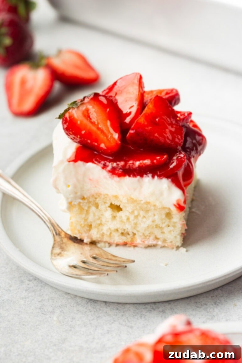 Simple Strawberry Shortcake 5 A photo of a tempting slice of strawberry shortcake cake resting on a small dessert plate, beautifully adorned with saucy halved strawberries. This classic dessert, featuring layers of moist vanilla cake, fresh strawberries, and whipped cream, is perfect for any celebration or a simple treat.