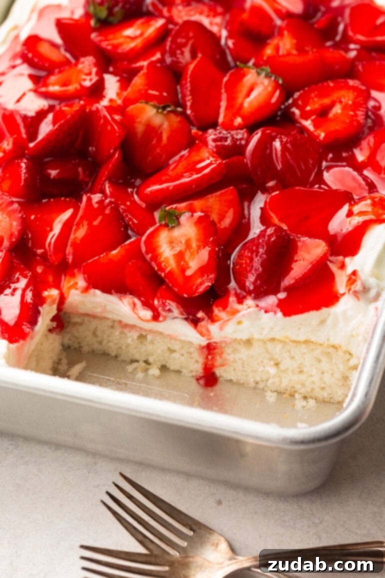 Simple Strawberry Shortcake 6 A captivating photo of a strawberry shortcake cake in a 9x13 inch metal cake pan, with a piece expertly removed from the corner to reveal the inviting cross-section of moist cake layers, creamy frosting, and juicy strawberries.