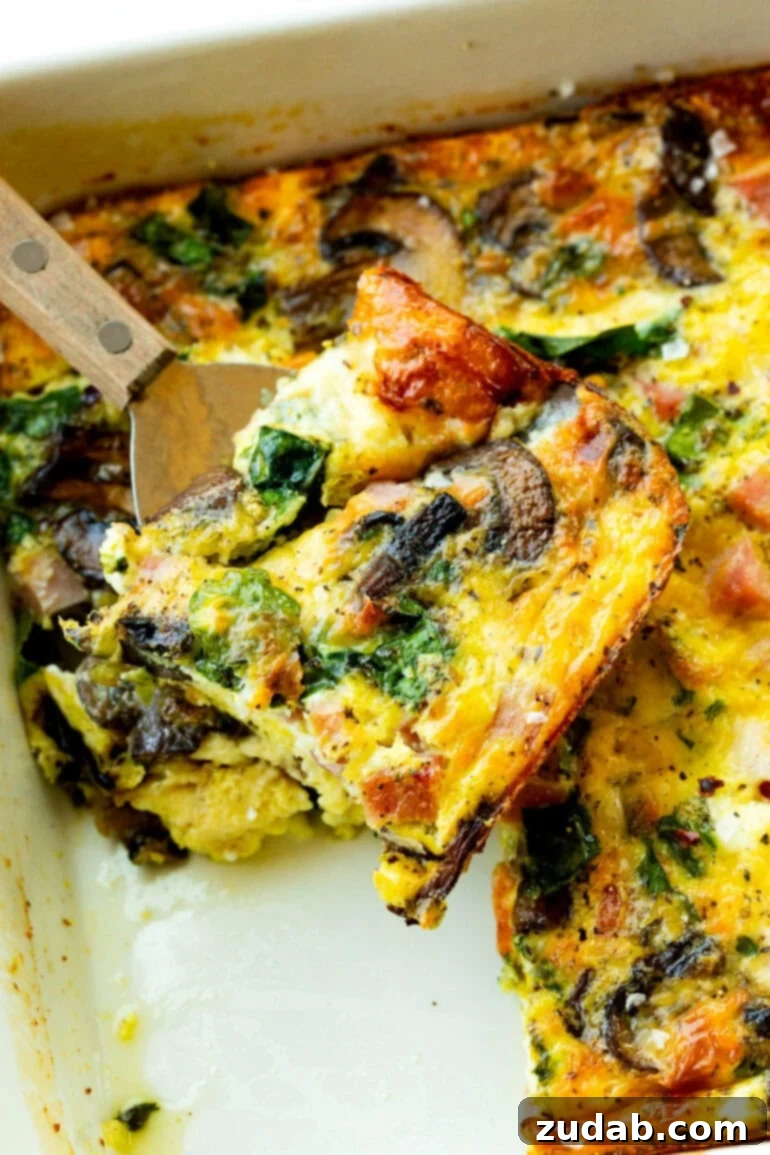 Morning Magic: Ham, Cheese, and Mushroom Egg Bake 7 A spatula lifting a piece of breakfast egg casserole from a pan.