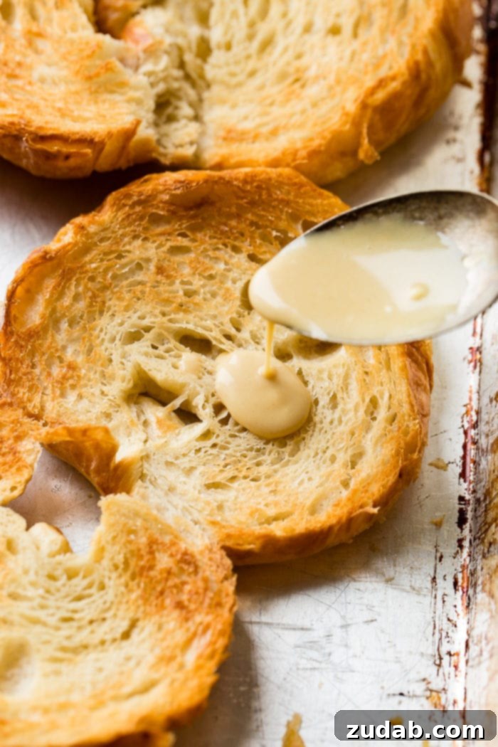 Bacon, Egg, and Cheese Croissant Breakfast Sandwiches 6 A photo of a toasted croissant half being drizzled with a rich, golden maple mustard sauce.