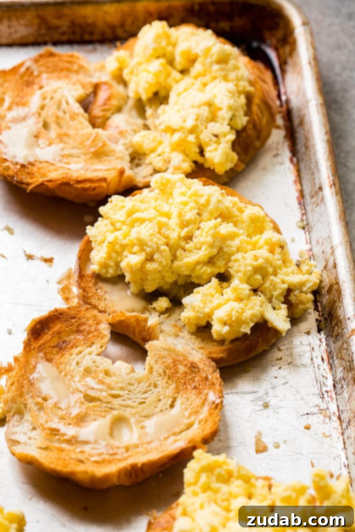 Bacon, Egg, and Cheese Croissant Breakfast Sandwiches 7 A photo of halved toasted croissants, with one half piled high with perfectly fluffy scrambled eggs.
