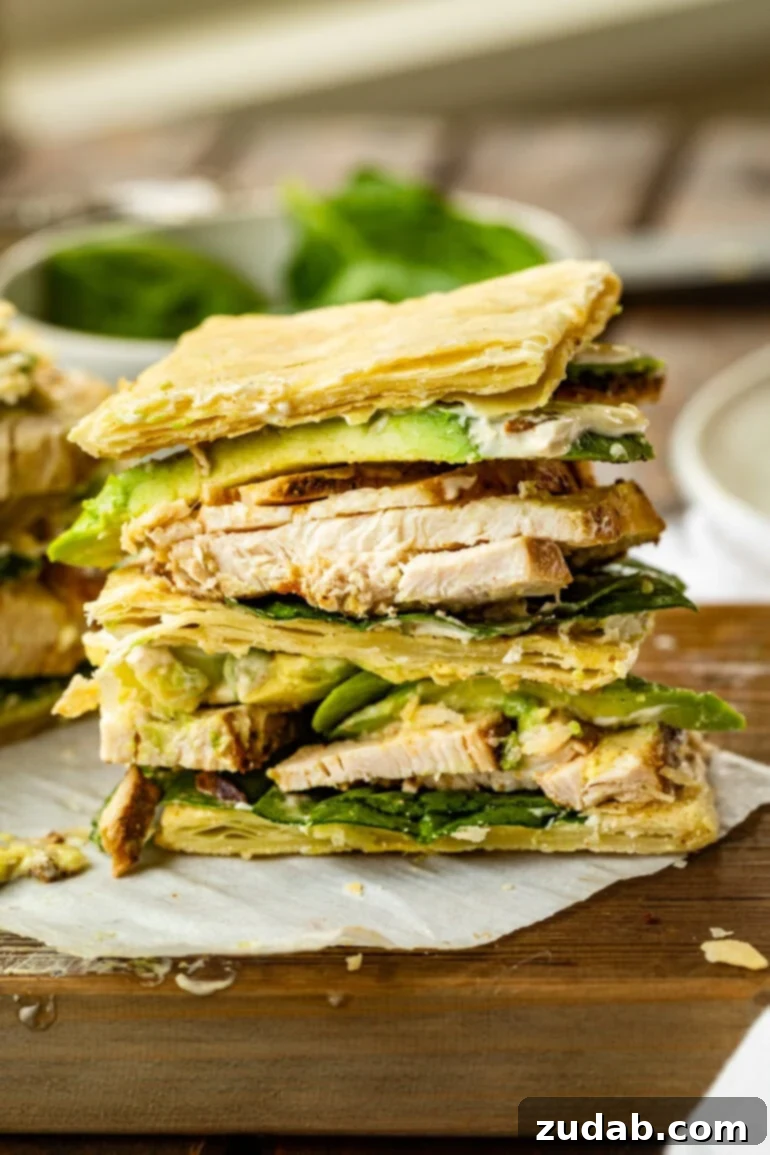Zesty Grilled Chicken Avocado Stack 3 A close-up photo of a grilled chicken and avocado puff pastry sandwich, sliced in half to reveal its beautifully layered interior with tender chicken, creamy avocado, fresh spinach, and a hint of spicy mayo.