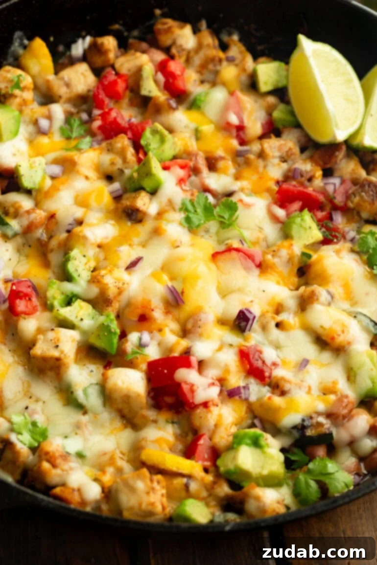 One-Pan Fiesta Chicken & Zucchini Skillet 3 Close-up of melted cheese generously blanketing chunks of seasoned chicken, vibrant tomatoes, fresh zucchini slices, and creamy avocado in a cast iron skillet.