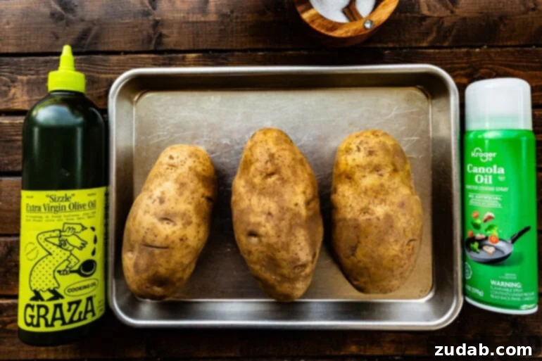 Ultimate Crispy Air Fryer Baked Potatoes 3 A few russet potatoes on a baking sheet, generously coated with olive oil and kosher salt, ready for the air fryer. This image highlights the simple preparation steps for achieving perfect crispy air fryer baked potatoes.