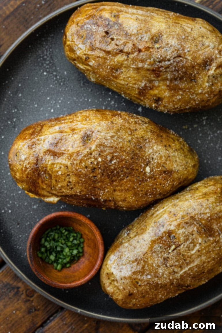 Ultimate Crispy Air Fryer Baked Potatoes 4 Close-up of crispy air fryer baked potatoes with perfectly salted skin, garnished with fresh chives and ready to be served. The golden-brown exterior promises a delightful crunch and fluffy interior.