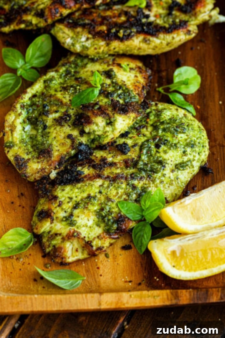 Golden Crispy Pesto Chicken 2 a photo taken over the top of two grilled chicken breasts coated in basil sitting on a cutting board with lemon wedges sitting next to them
