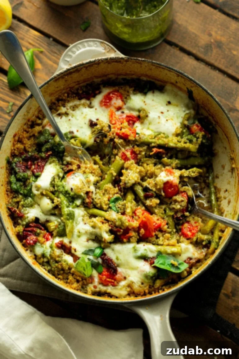 Pratik Tek Tavada Pesto Kuşkonmazlı Kinoa 2 a photo of a cast iron skillet of quinoa mixed with pesto, asparagus, tomatoes and topped with melted cheese
