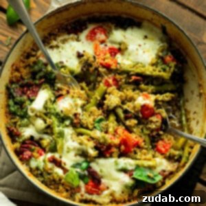 a photo of a cast iron skillet of quinoa mixed with pesto, asparagus, tomatoes and topped with melted cheese