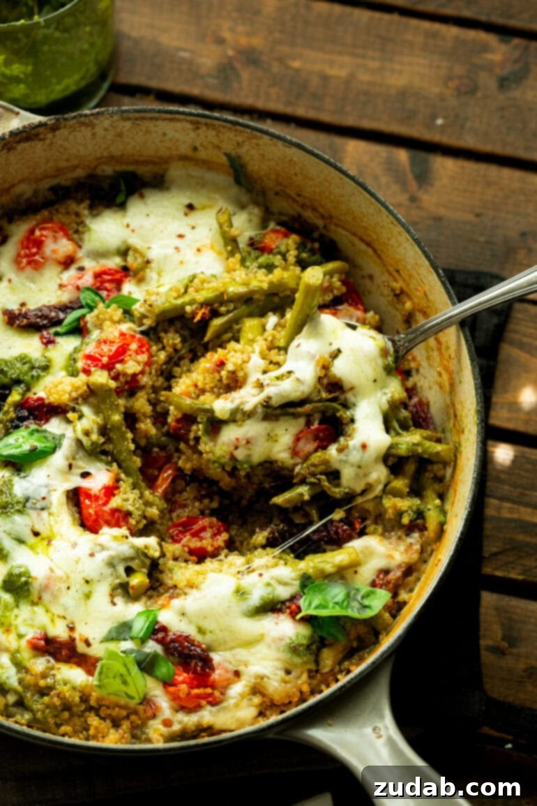 Pratik Tek Tavada Pesto Kuşkonmazlı Kinoa 4 a photo of a cast iron skillet filled with pesto quinoa mixed with asparagus spears, roasted tomatoes and topped with melted mozzarella cheese