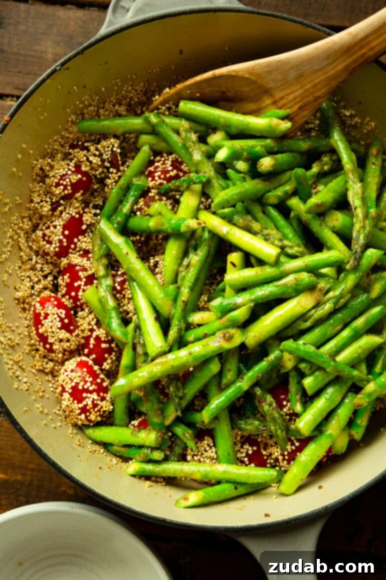 Pratik Tek Tavada Pesto Kuşkonmazlı Kinoa 6 a photo of a skillet with uncooked quinoa mixed with cherry tomatoes topped with spears of bright green uncooked asparagus