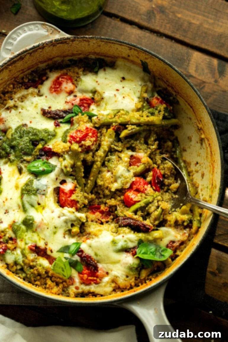 Pratik Tek Tavada Pesto Kuşkonmazlı Kinoa 7 a photo of a skillet of asparagus pesto quinoa topped with melted mozzarella and whole fresh basil leaves being scooped up with a silver serving spoon