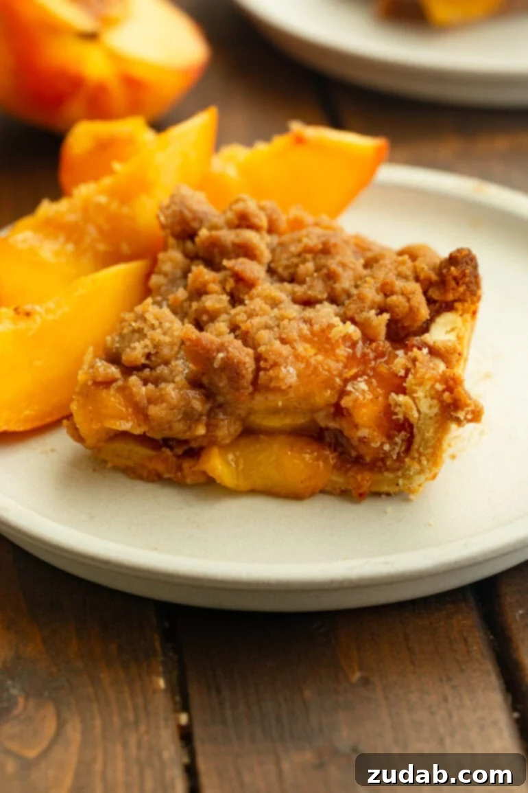 Golden Peach Crumble Squares 2 A slice of peach crumble bar on a white plate, topped with golden-brown streusel and served with fresh peach slices.