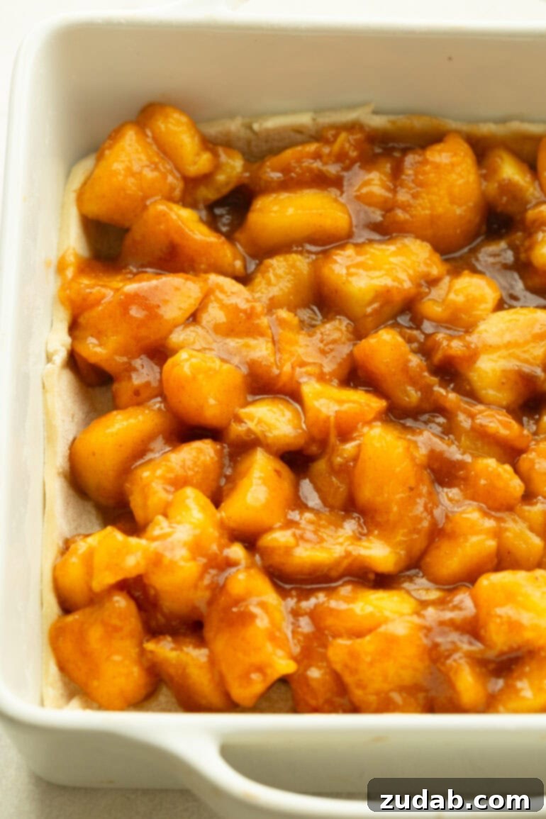 Golden Peach Crumble Squares 4 Close-up of baked peach filling in a white baking dish, showing soft, juicy peach chunks coated in a glossy cinnamon-sugar sauce.