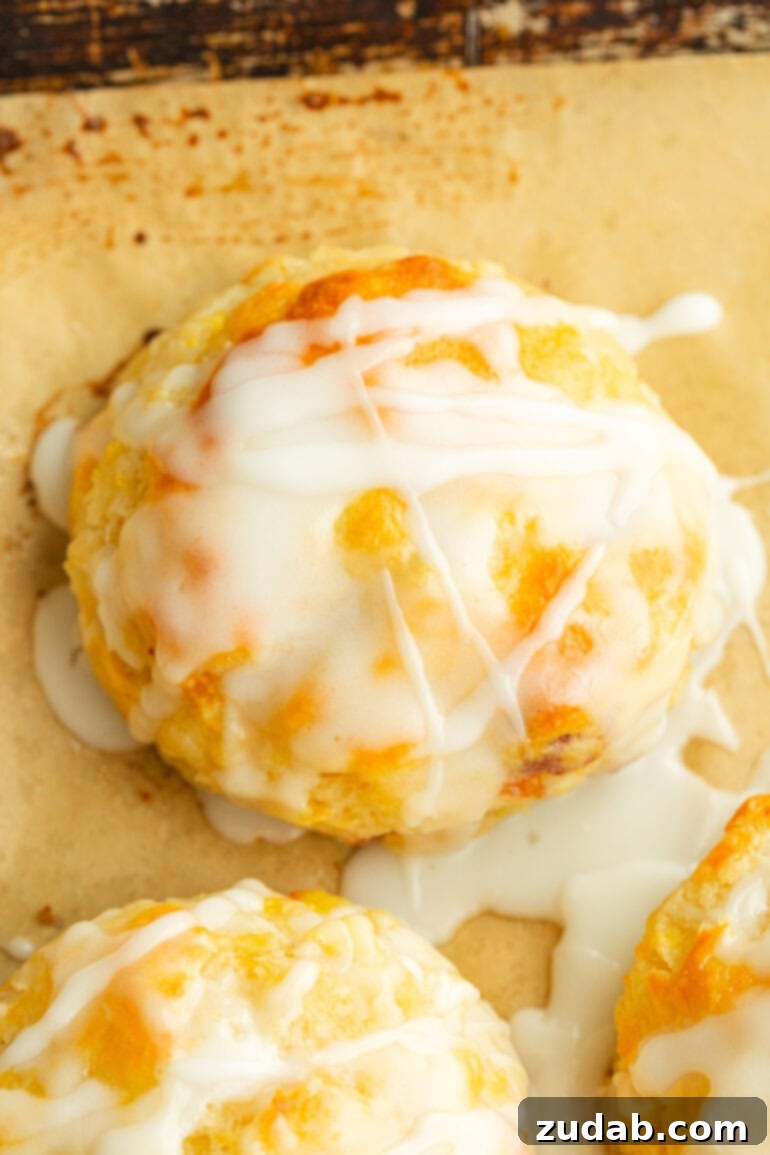 Sun-Kissed Peach Buttermilk Biscuits 5 A close-up of a golden brown biscuit, showing visible chunks of juicy peach within its flaky structure, with a smooth glaze generously dripping down its sides.