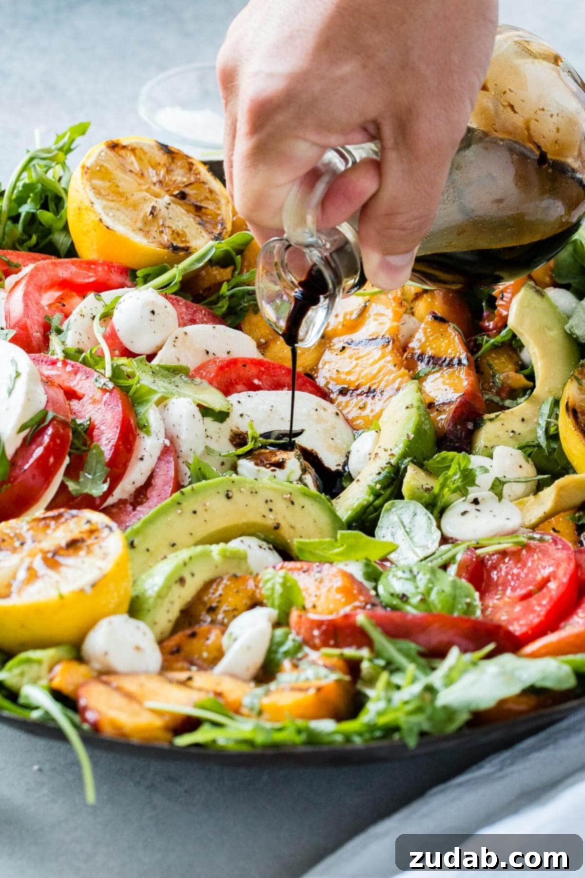 Grilled Peach Caprese 6 A hand drizzling balsamic glaze over the stunning grilled peach caprese avocado salad, showcasing its delicious finish and vibrant colors.