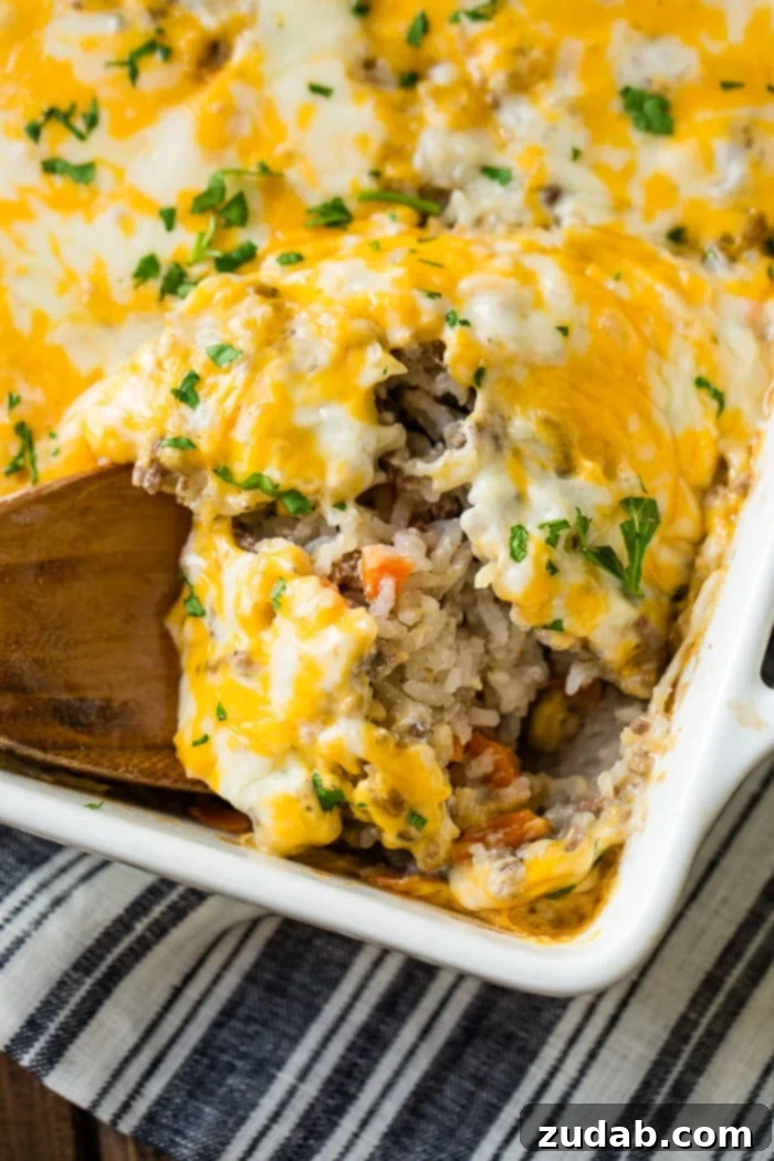 Golden Cheesy Beef & Rice Bake 4 A gleaming white ceramic casserole dish filled with a savory ground beef, rice, and carrot casserole, generously topped with glistening melted Colby Jack cheese and sprinkled with fresh parsley for an inviting garnish.
