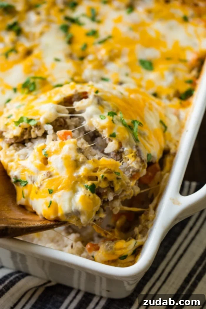 Golden Cheesy Beef & Rice Bake 5 A rustic wooden spoon gently scooping a portion of the warm, cheesy ground beef, rice, and carrot casserole, highlighting its rich texture and melted cheese topping.