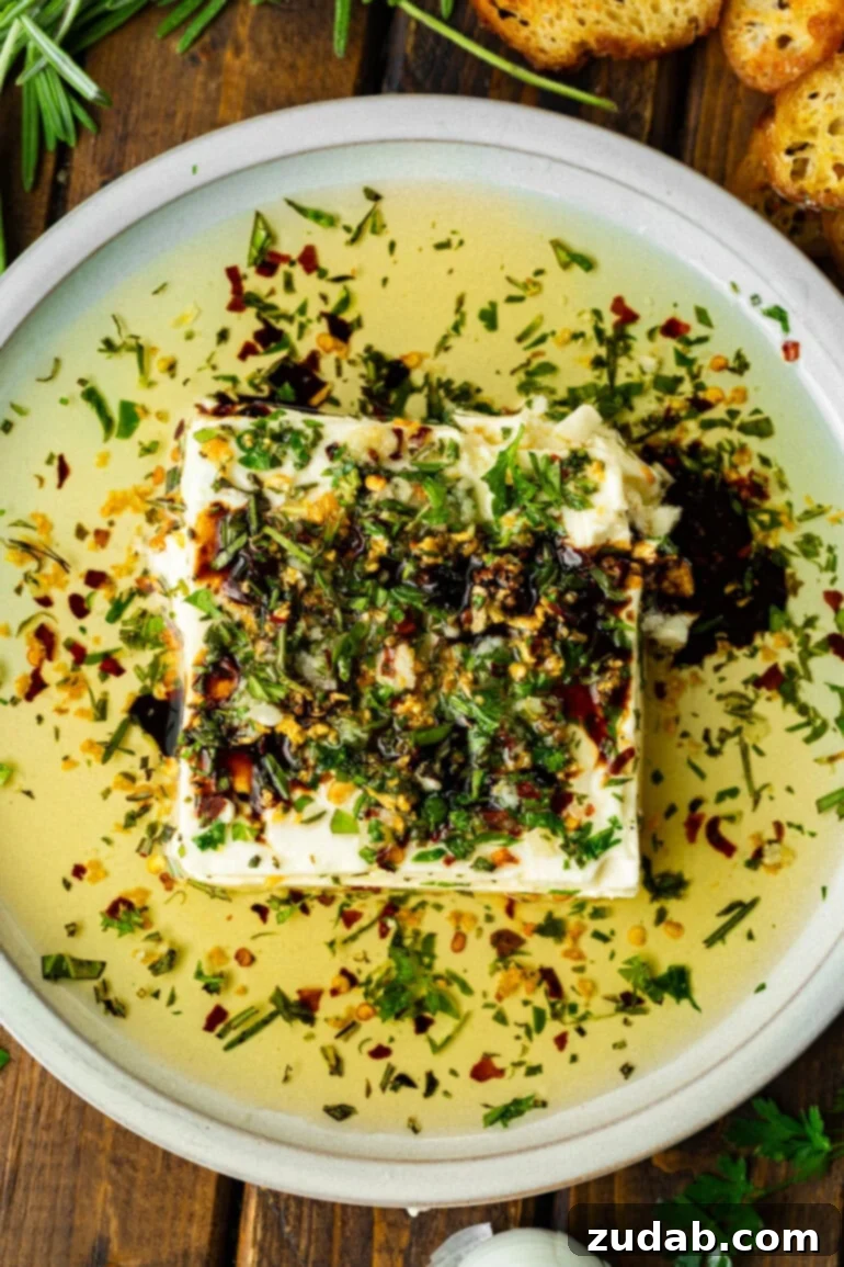 a shallow white circular serving tray with a block of feta cheese topped with sizzling herb oil