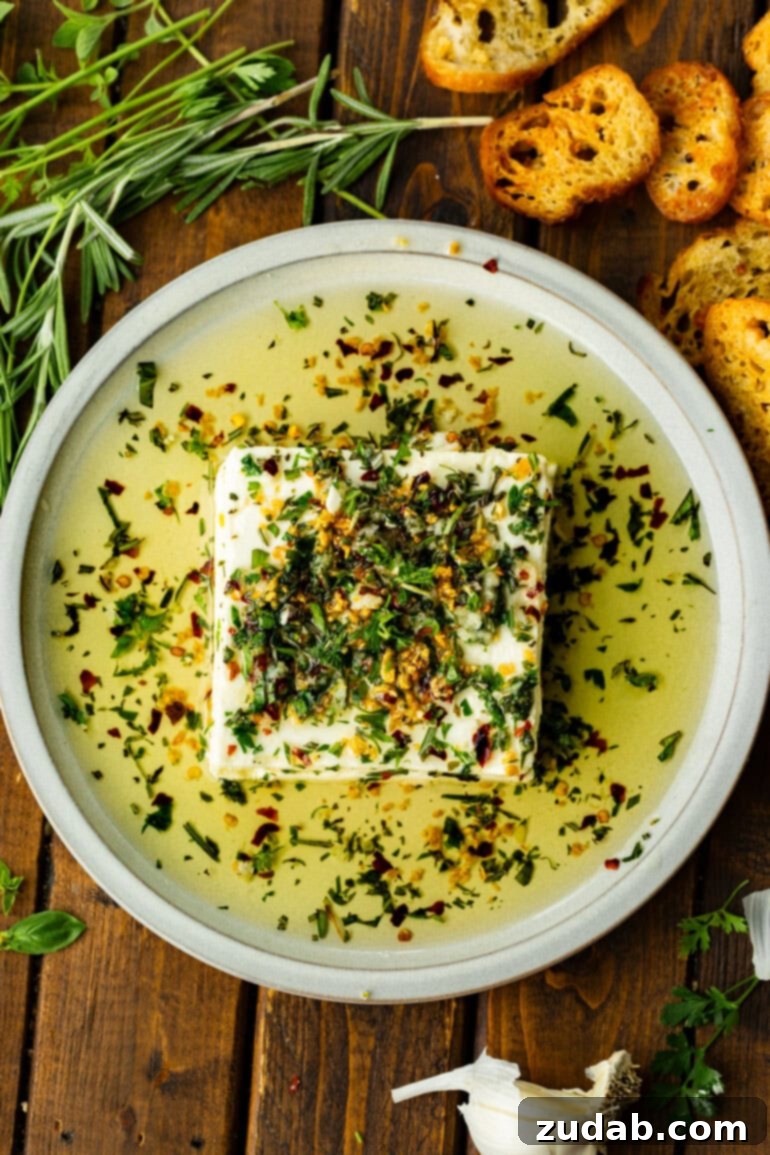 a square brick of feta cheese sitting on a serving plate in a pool of herby olive oil