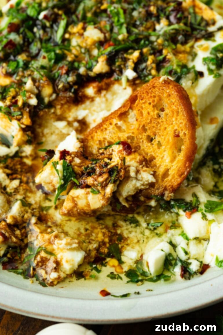 a photo of a crostini dipped in a bowl of creamy feta topped with hot herb oil