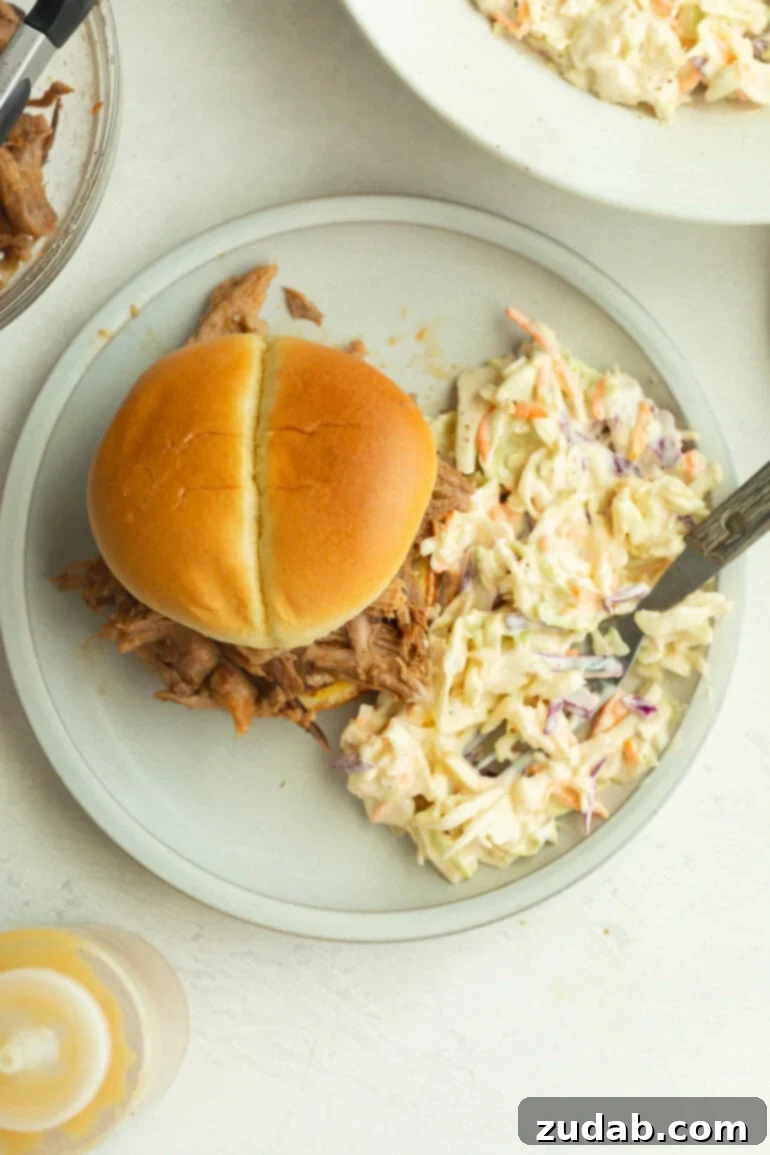 The Secret to Amazing Homemade Coleslaw 3 A perfect pulled pork sandwich topped with creamy summer coleslaw featuring shredded green cabbage and carrots, dressed in a smooth, flavorful mixture.