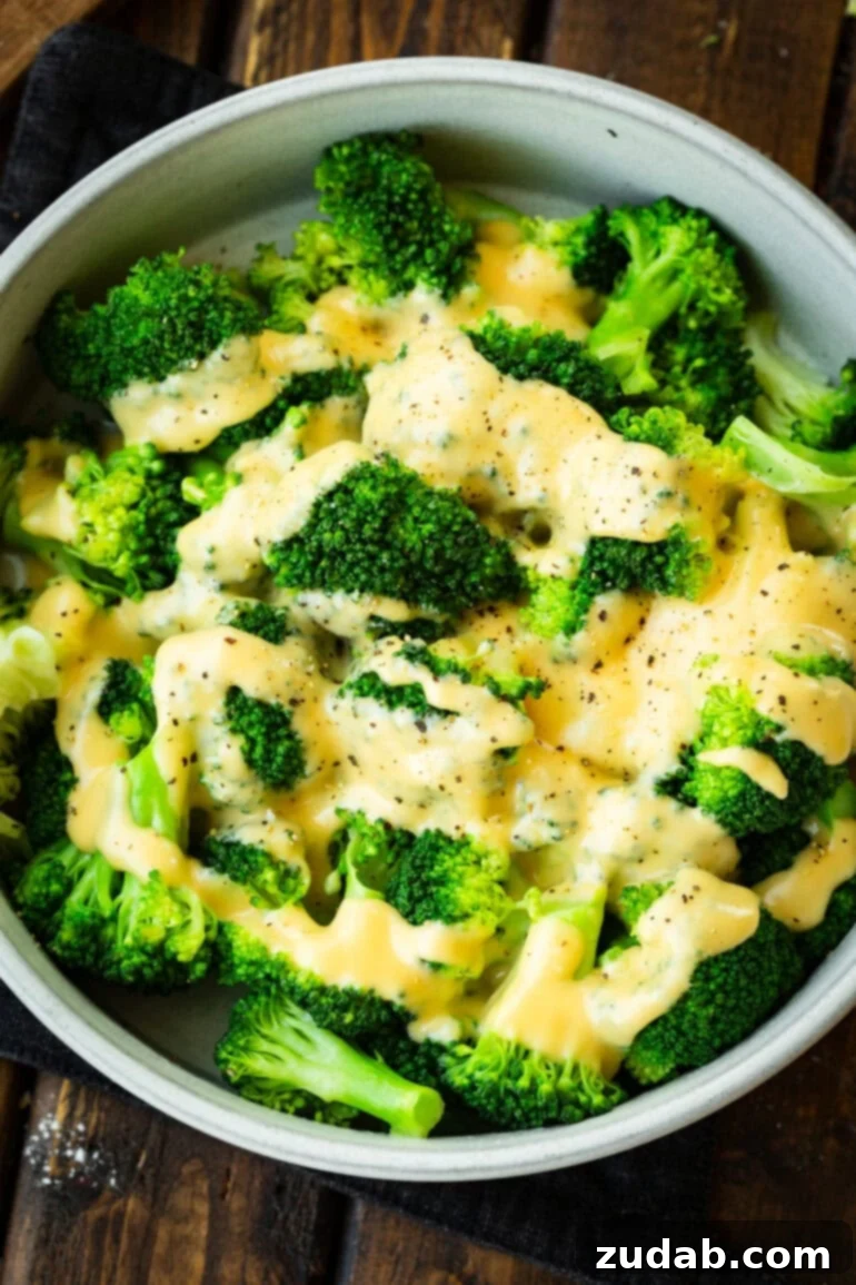 a large bowl of bright green steamed broccoli topped with cheddar cheese sauce and salt and pepper