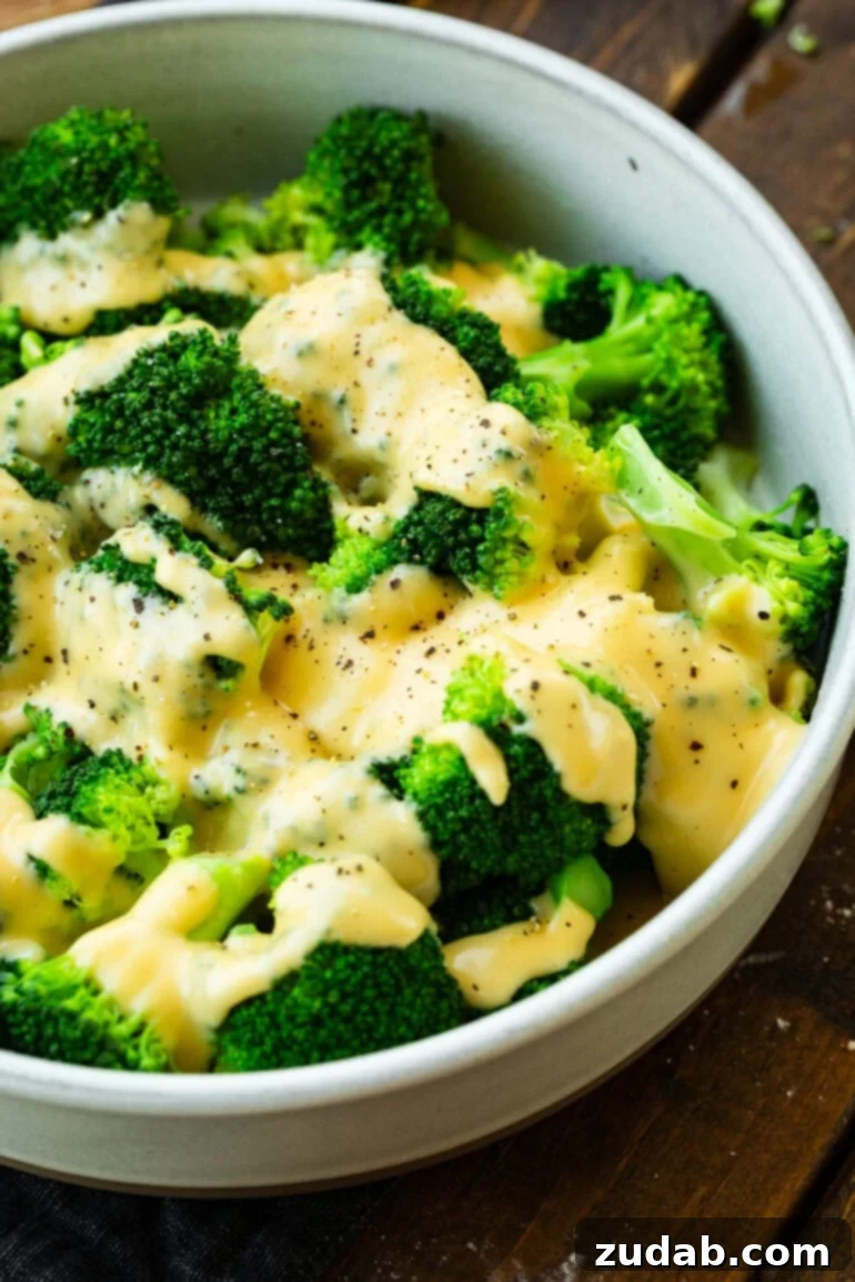 a photo of a large bowl of fresh steamed broccoli topped with creamy cheese sauce and cracked pepper
