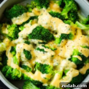 a photo of a large bowl of bright green steamed broccoli topped with a creamy cheese sauce and sprinkled salt and pepper