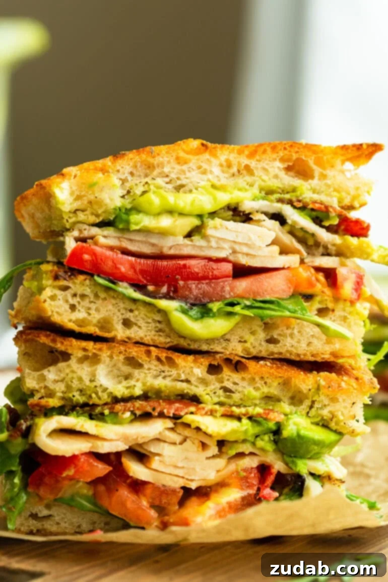 Honey Avocado Turkey Bacon Sandwich 2 A freshly made Turkey Bacon Avocado Sandwich, cut in half to showcase layers of turkey, crispy bacon, creamy avocado, and sliced tomatoes, served on rustic bread.