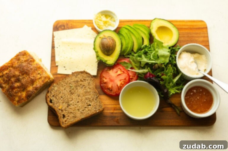 Honey Avocado Turkey Bacon Sandwich 4 All the fresh ingredients for a Turkey Bacon Avocado Sandwich, including sliced turkey, crispy bacon, ripe avocados, tomatoes, mixed greens, and honey avocado sauce, neatly arranged on a wooden cutting board.