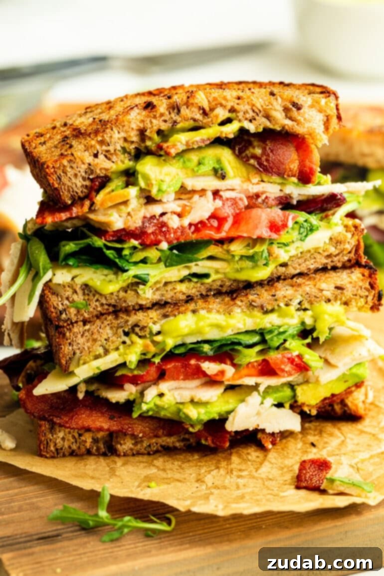 Honey Avocado Turkey Bacon Sandwich 10 Two halves of a Turkey Bacon Avocado Sandwich, stacked artfully to show the cross-section of layers, including multigrain bread, turkey, bacon, avocado, and tomato.