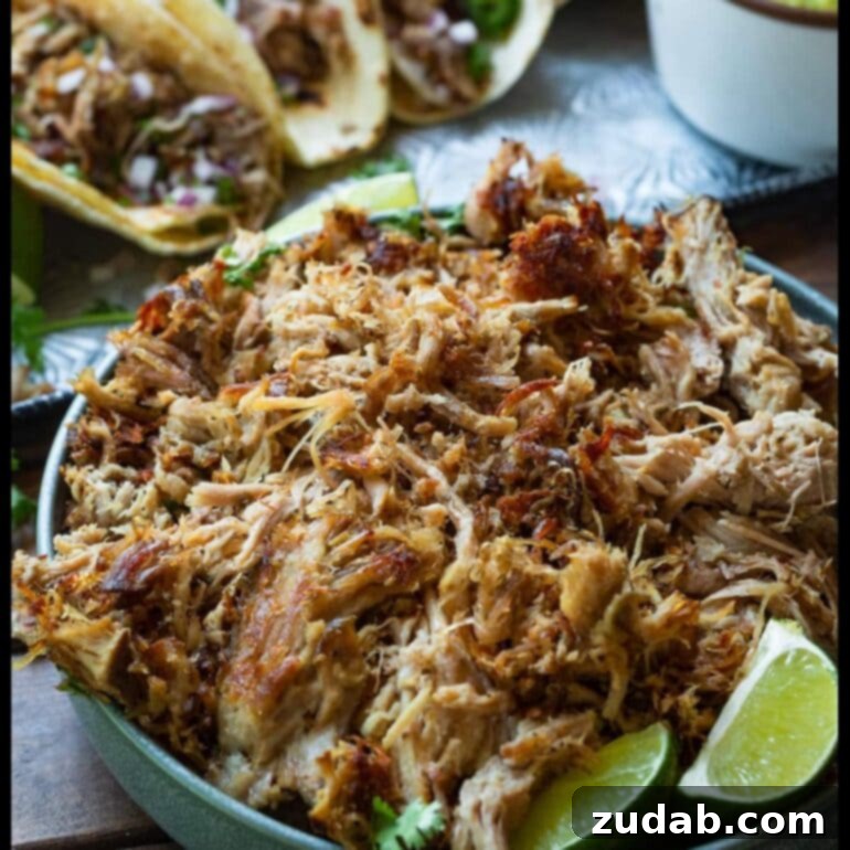 Close-up of crispy and tender pork carnitas with lime wedges and cilantro
